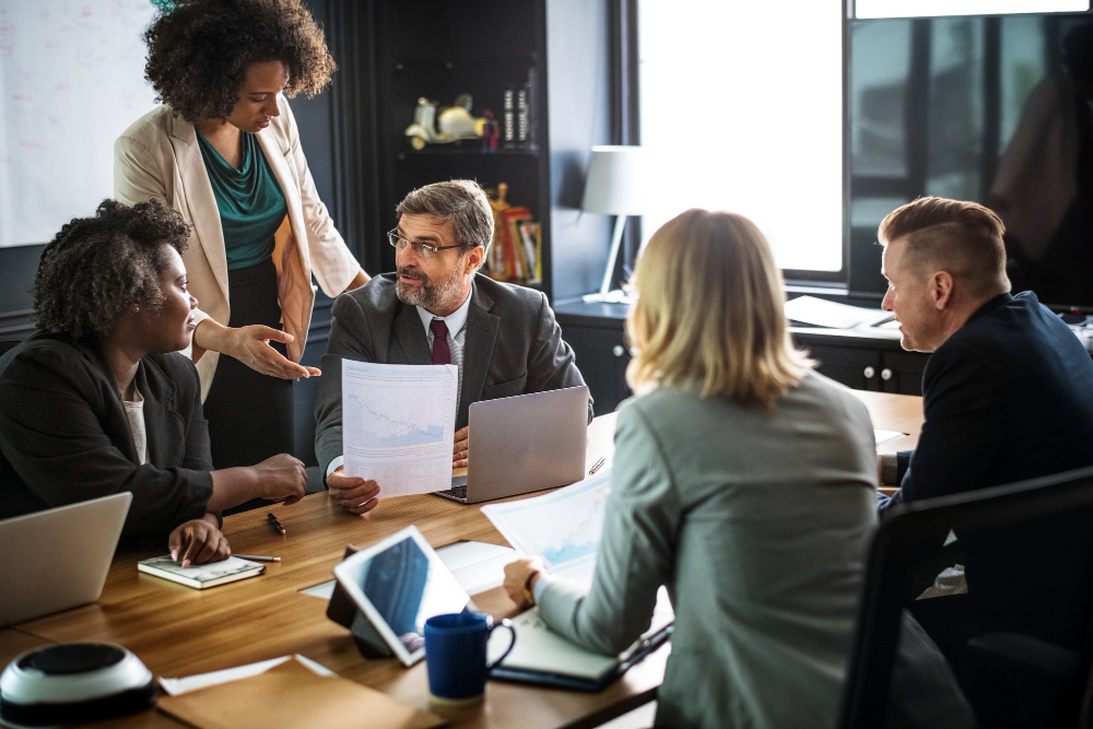 Profissionais reunidos analisando documentos e gráficos em uma reunião empresarial, representando a identificação do CNAE correto para uma atividade.