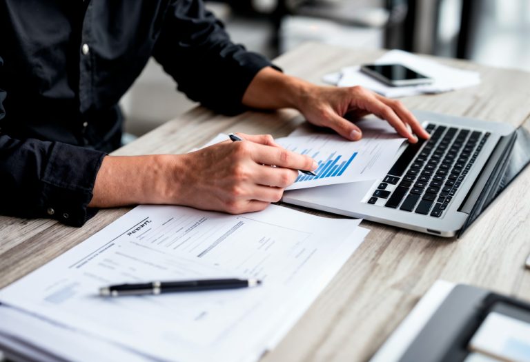 Profissional analisando gráficos e documentos financeiros ao lado de um notebook, representando a contabilidade para afiliados digitais.