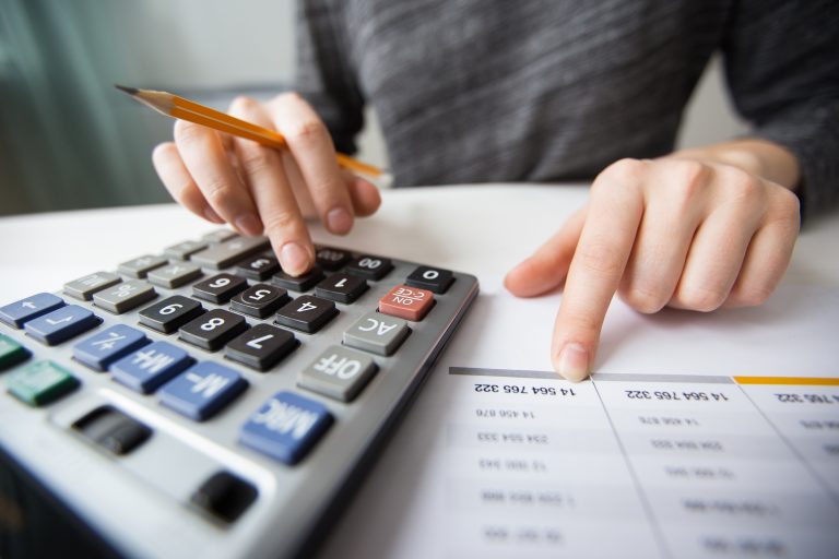 Pessoa utilizando uma calculadora e analisando uma planilha financeira, representando o cálculo de impostos de um afiliado digital no Brasil.